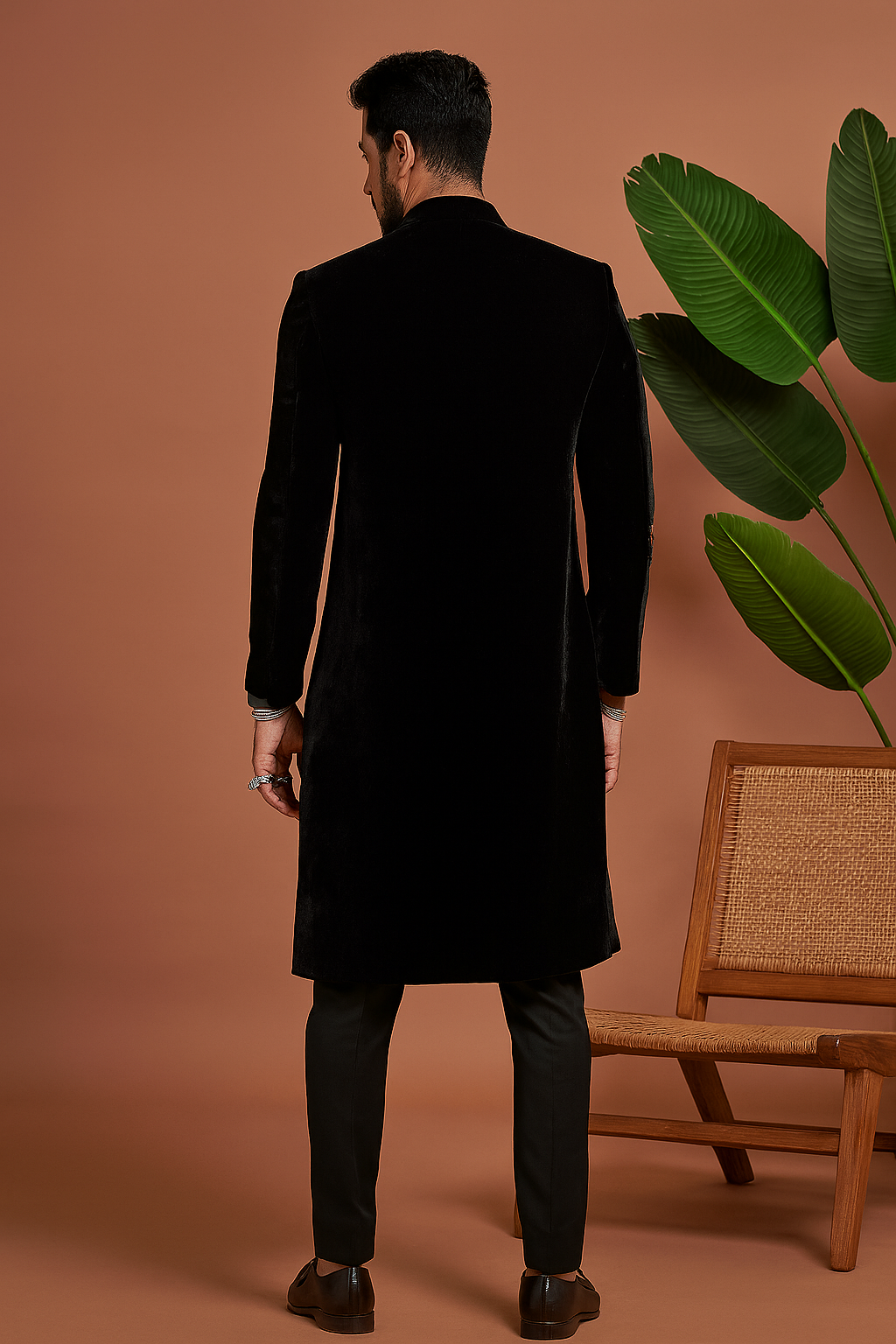 modern silhouette. He is standing and posing confidently in a studio setting with a plant in a pot visible behind him 