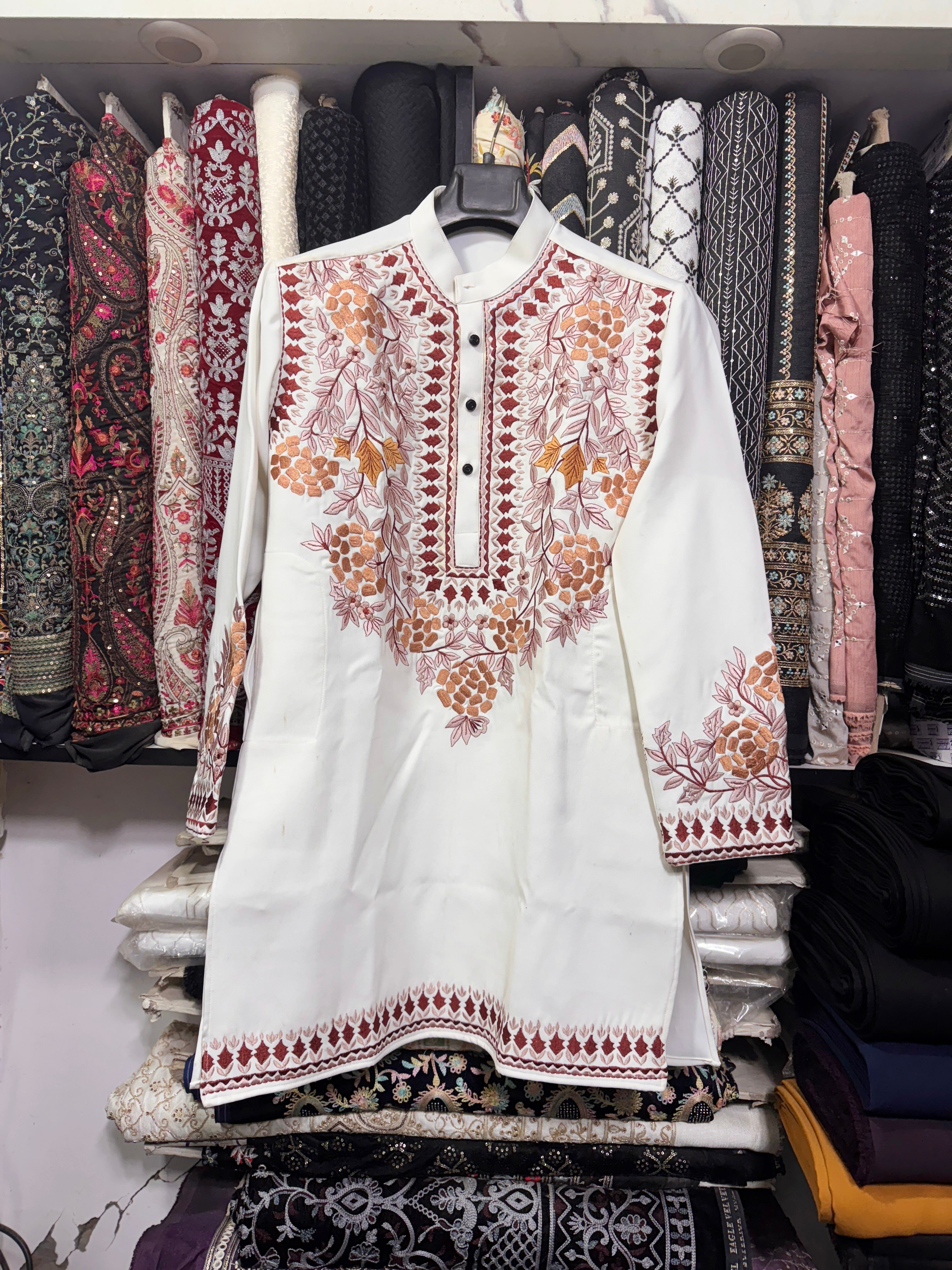 White embroidered shirt on a rack with patterned fabrics in the background